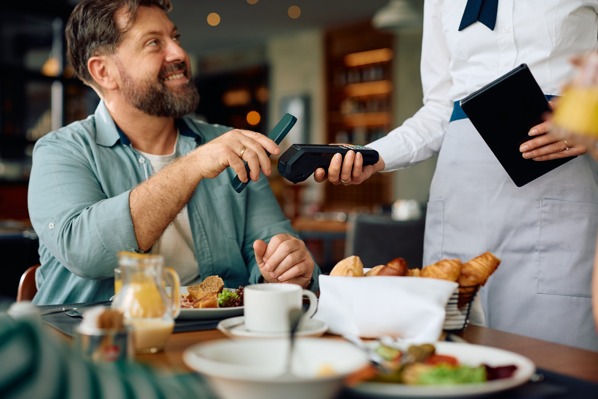 Close up of man paying contactless after having a breakfast in restaurant.